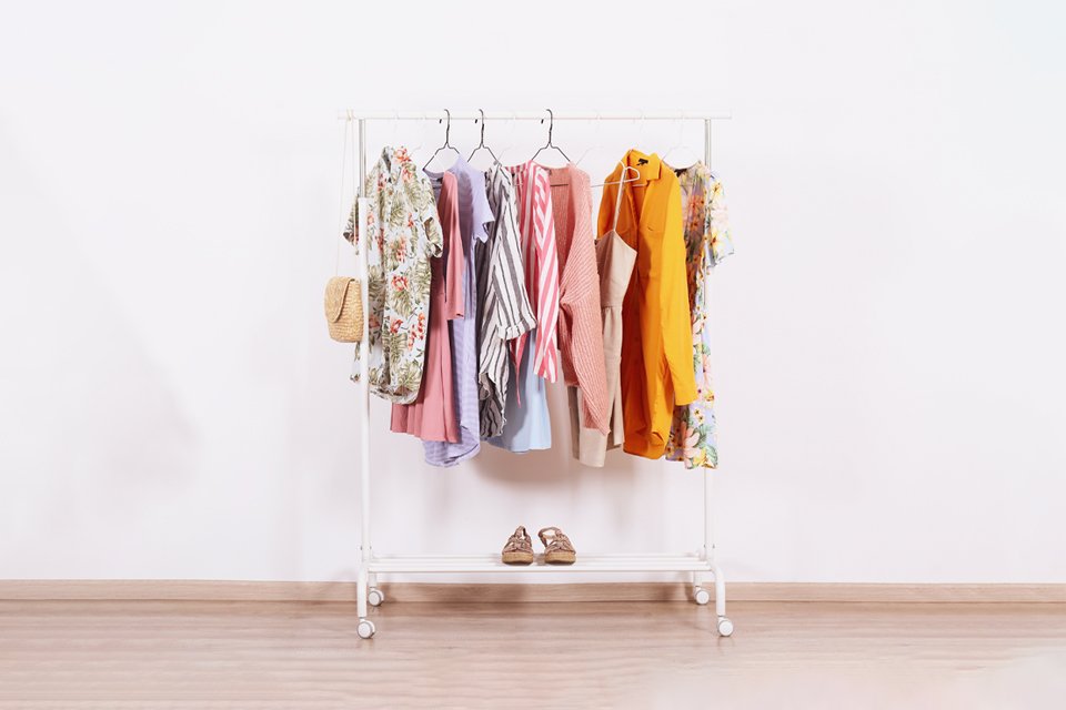 A white clothing rail with colourful clothes hanging on it.
